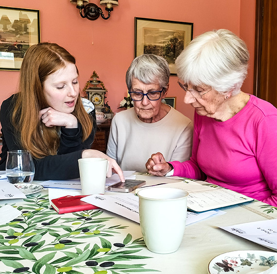 The Acorn Project - two older women and a GRCC staff member drinking tea and practising using a smartphone at a DAISI event